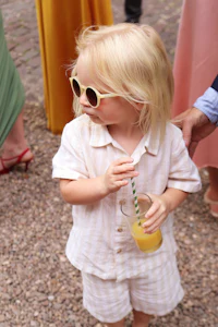 a little girl wearing sunglasses and holding a drink