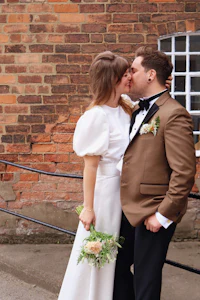 a bride and groom kissing in front of a brick wall