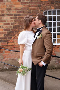 a bride and groom kissing in front of a brick wall