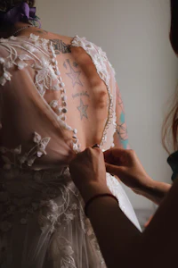 a woman putting on a wedding dress with tattoos on her back
