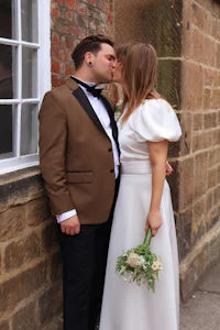 a bride and groom kissing in front of a brick wall